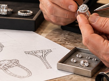Jeweler inspecting a diamond ring beside design sketches